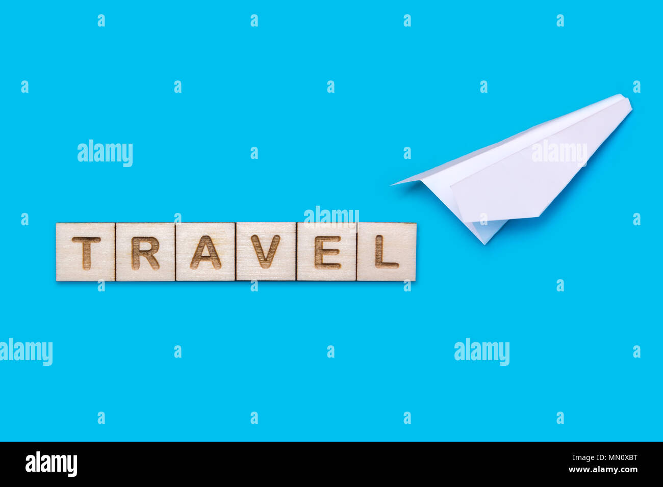 Konzept auf das Thema der Reise. Weiß origami Flugzeug auf einem blauen Hintergrund. Das Wort Reisen aus Holz Bausteine gelegt wird. Stockfoto