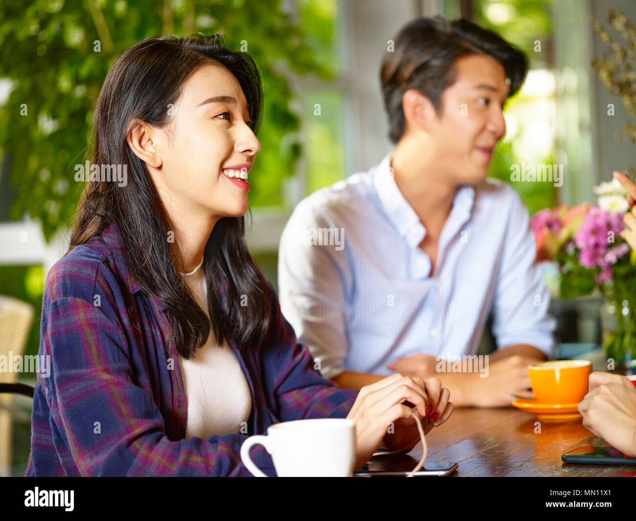 Glückliche junge asiatische Mann und Frau im Gespräch mit Freunden im Café Stockfoto