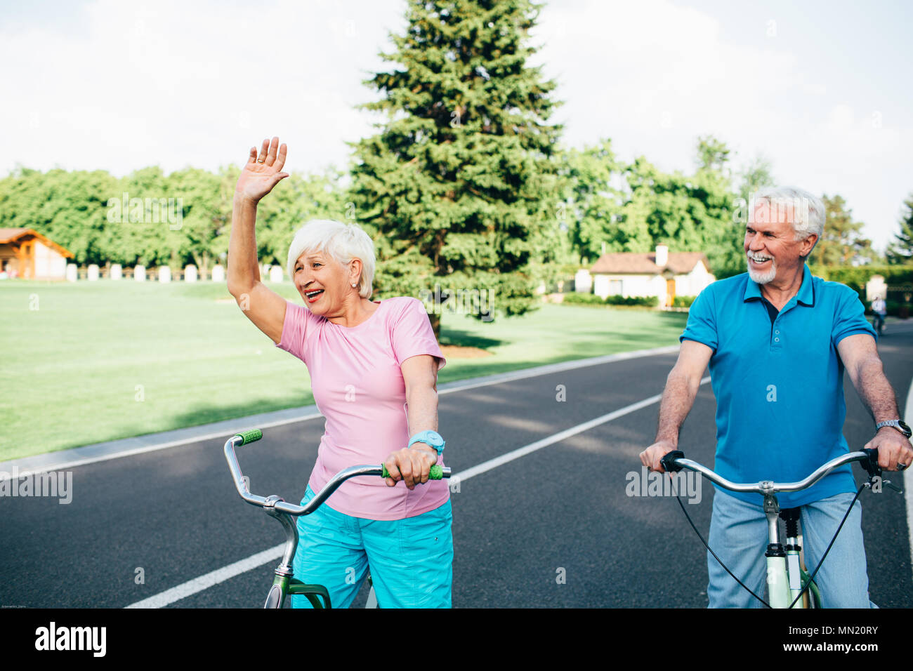 Positive senior Paar Fahrrad fahren im sonnigen Park. ältere Frau aktiv gestikuliert während Radfahren Stockfoto