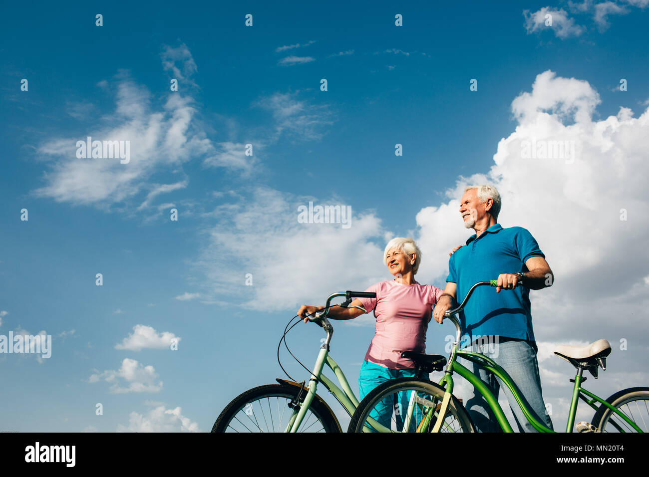 Senior Paar mit ihrer Fahrräder stehen gegen den blauen Himmel und schauen weg, Seitenansicht Stockfoto