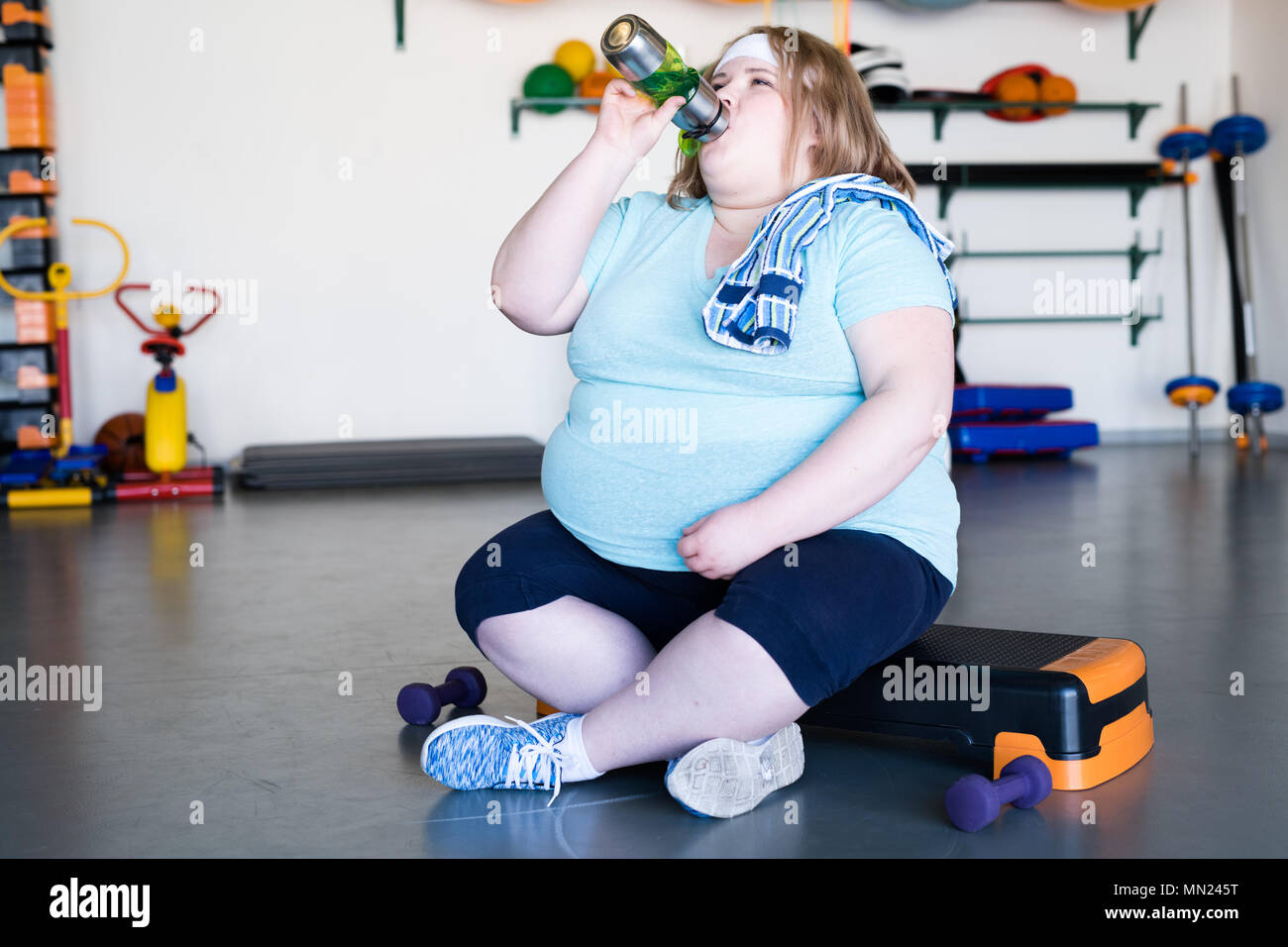 Volle Länge Portrait von erschöpft beleibte Frau sitzt auf Schritt und Trinkwasser nach extremen weightloss Workout im Fitness Club, Platz kopieren Stockfoto