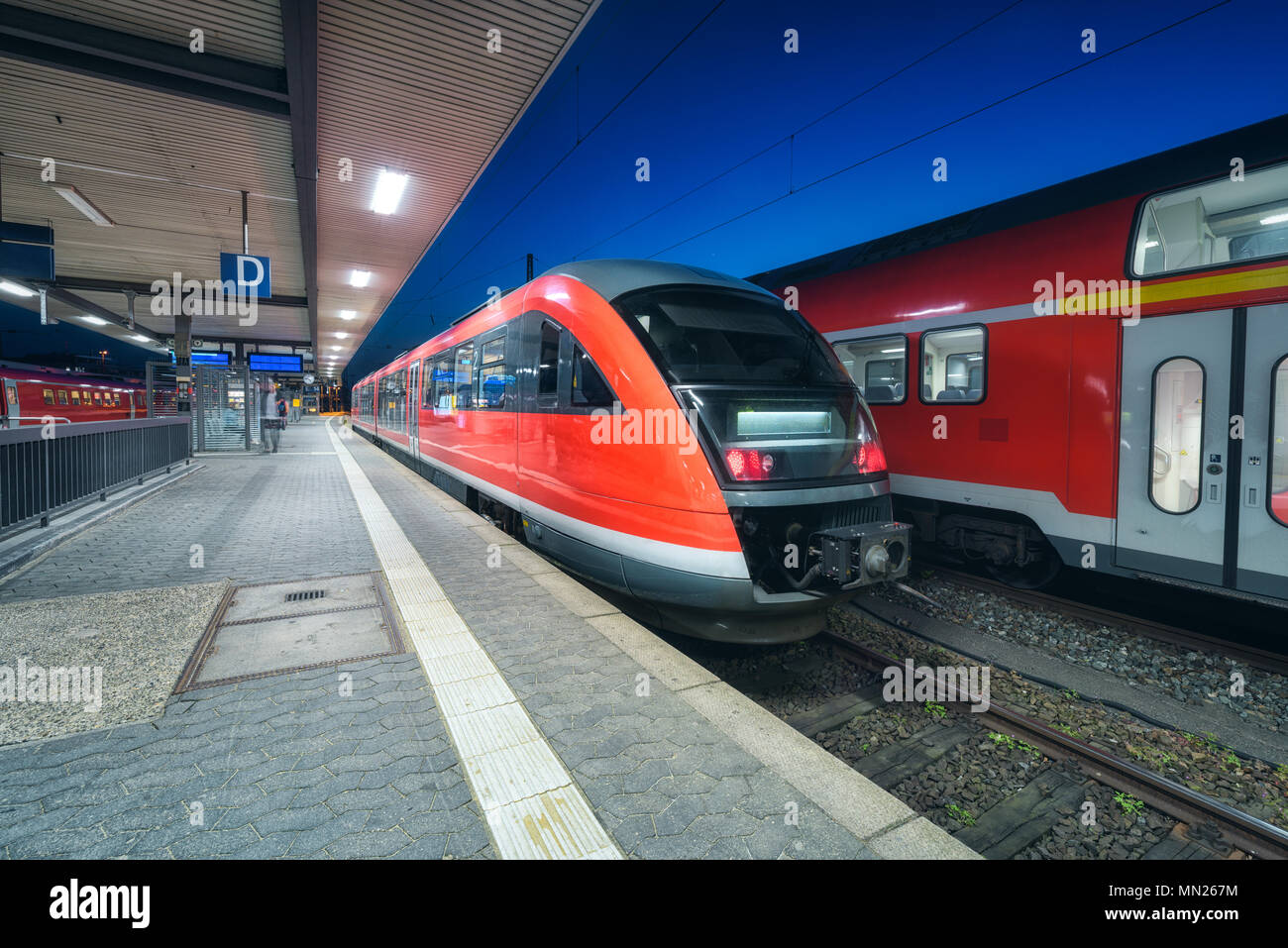 Hochgeschwindigkeitszug auf dem Bahnhof in der Nacht in Nürnberg, Deutschland. Moderne Intercity Zug auf dem Bahnsteig mit illumintain. Pendler rot Stockfoto