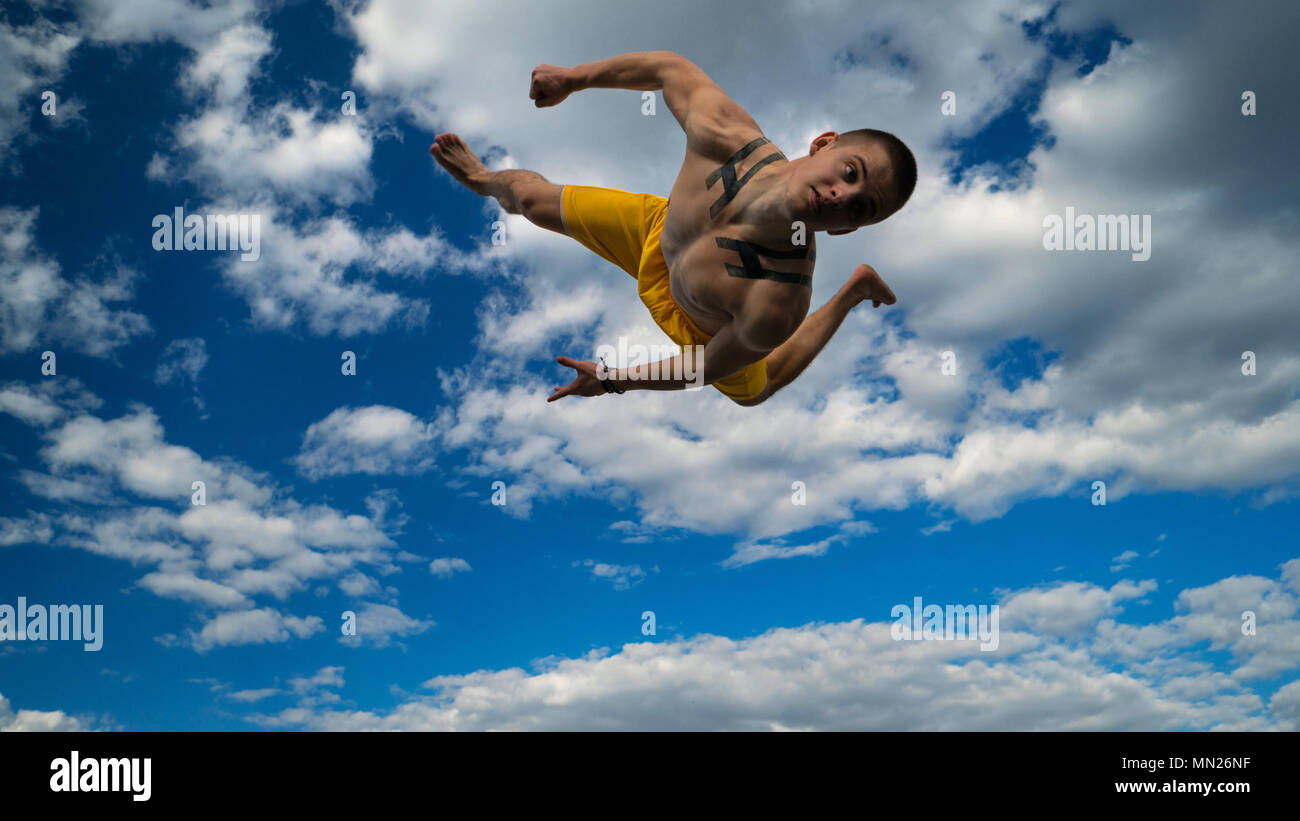 Austrickst, auf die Straße. Kampfsportarten Mann führt Salto vor barfuß. Bhudda Verkürzungen von unten gegen den Himmel. Stockfoto