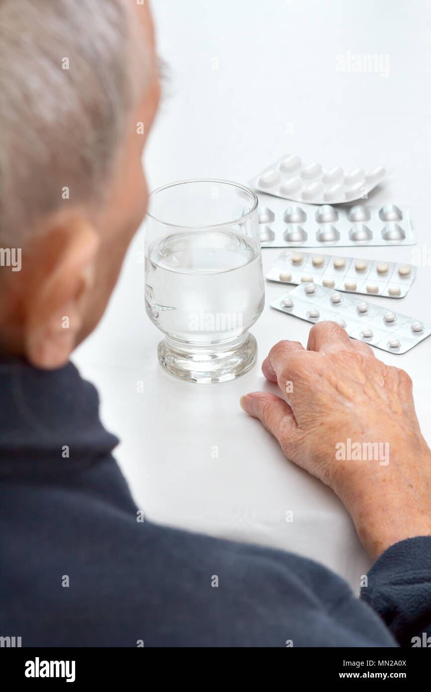 Alte Frau an einem Tisch, in der Küche oder im Wohnzimmer mit einem Glas Wasser und verschiedene Tabletten in Blisterpackungen sitzen Stockfoto