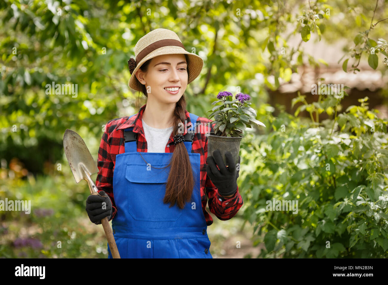 Gärtner in Arbeitskleidung holding Blume im Topf und kleinen Spaten Stockfoto