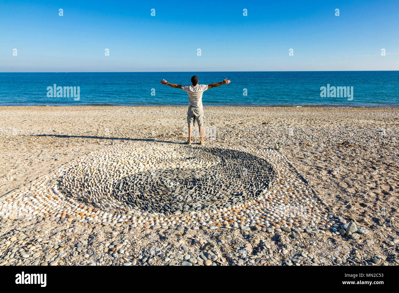 Erde Kunst am Strand von Palavas-les-Flots (Südfrankreich): Yin und Yang Symbol mit Kieselsteinen am Strand und Mann gesehen von hinten, Arme erstellt Ausdrucke Stockfoto