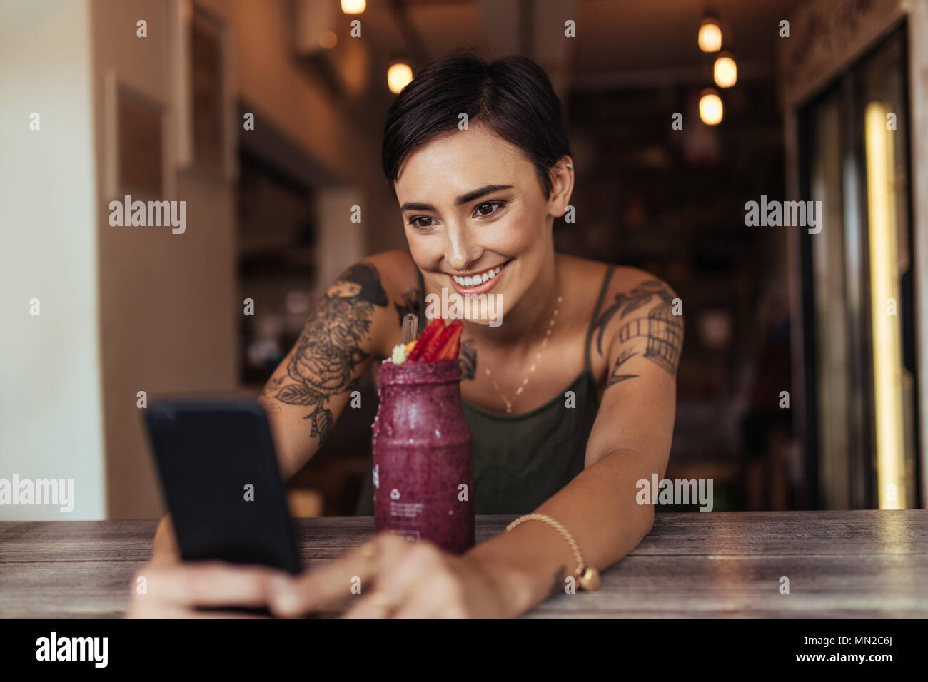 Lächelnde Frau mit einem selfie mit einem Smoothie vor ihr Handy für ihr Essen blog platziert. Essen blogger Fotografieren für Ihren Blog. Stockfoto