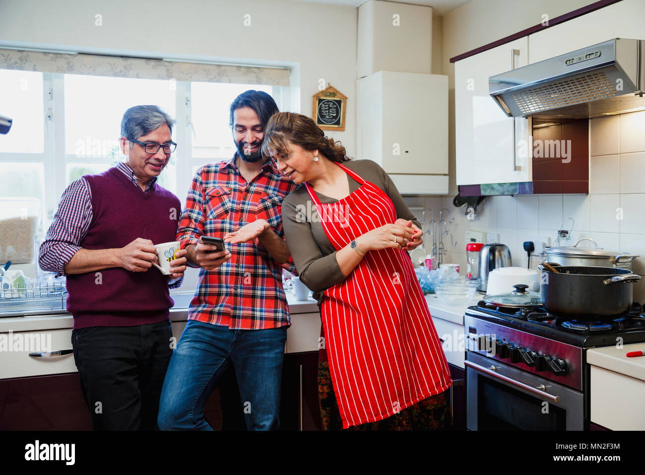 Mitte der erwachsenen Mann ist, der seine Eltern etwas auf seinem Smartphone, während Sie in der Küche Ihres Hauses sind. Stockfoto