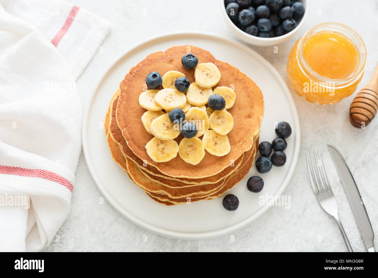 Hausgemachte Pfannkuchen mit Heidelbeeren und Banane auf weiße Platte. Stapel von Mais Pfannkuchen. Pfannkuchen mit Früchten und Honig auf einem Tisch Stockfoto