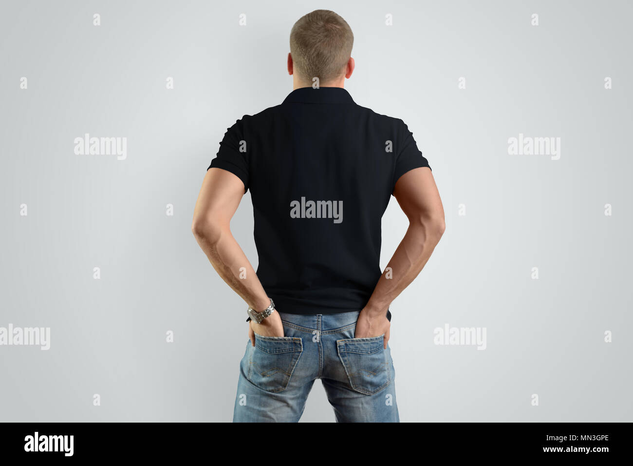 Zurück Mockup schwarz Poloshirt auf ein männliches Modell für ein Beispiel. Mann mit den Händen in den Taschen hinten auf grauem Hintergrund. Stockfoto