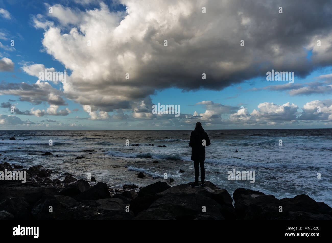 Rolling cloudscape über die Silhouette eines ständigen Mann vor der Meereswellen Stockfoto