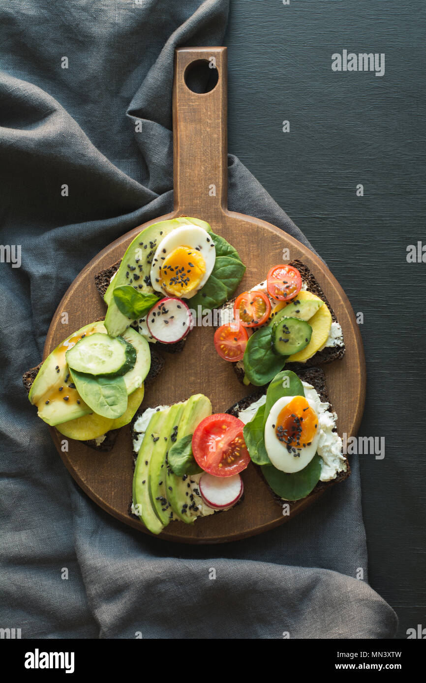 Verschiedene Sandwiches mit Gemüse, Eier, Avocado, Tomate, Roggenbrot auf schwarzem Hintergrund auf dem Schwarzen Brett. Blick von oben. Appetizer für Party. Flach. Stockfoto