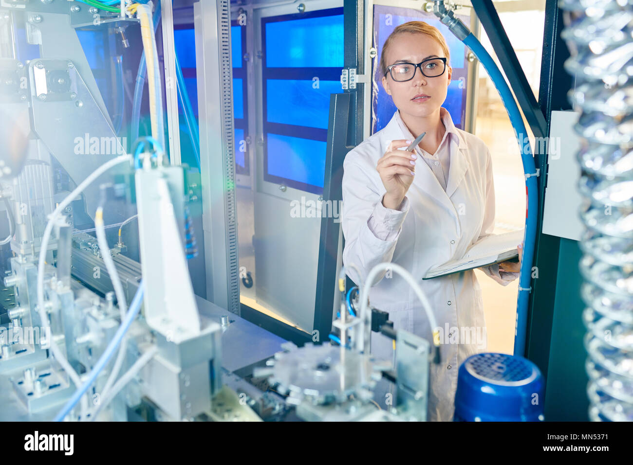 Portraitfotos der überzeugten Techniker tragen weiße Fell und Brillen holding Notizblock und Stift in der Hand, während conducing Inspektion der moderne Fabrik Stockfoto