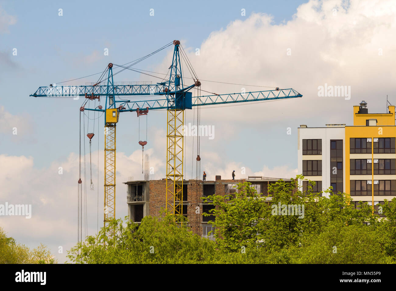 Stadtentwicklung Blick auf die Silhouetten von zwei hohen industriellen Turmdrehkrane am Bau neuer Ziegelgebäude mit Arbeitern in harte Hüte sie daran arbeiten und gegen BR Stockfoto