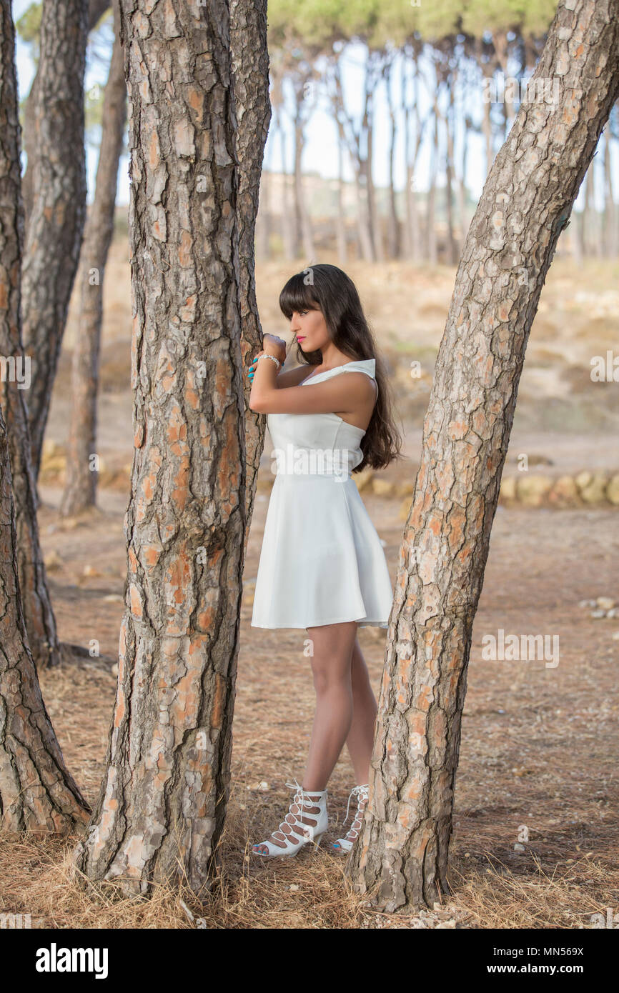 Schöne Frau trägt ein weißes Kleid gegen einen Baum im Wald weg schauen Schiefen Stockfoto