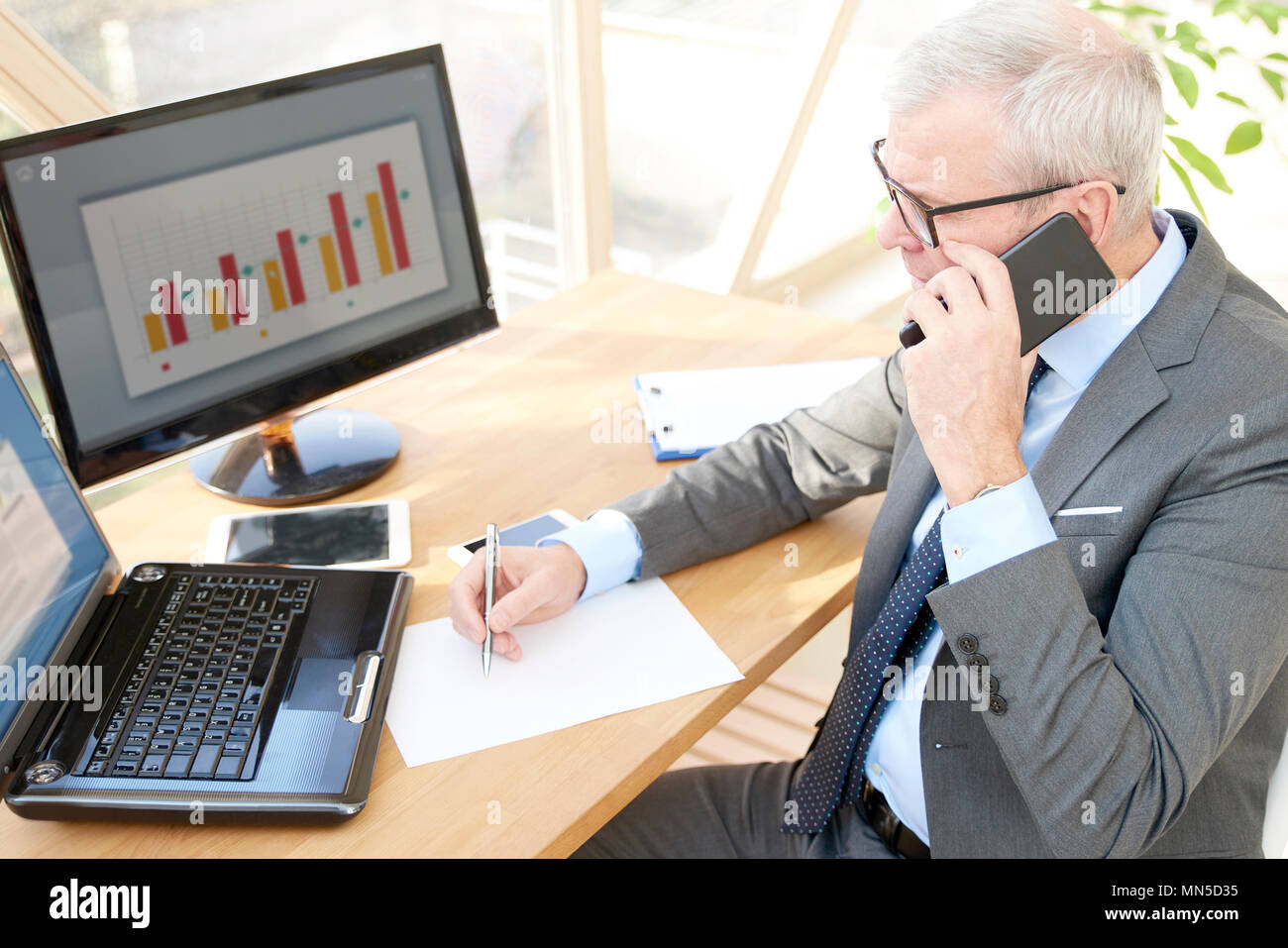 Hohe Aufnahme von Senior Investment Geschäftsmann tragen Anzug, während im Büro Schreibtisch vor dem Laptop sitzen und zum Telefonieren. Stockfoto