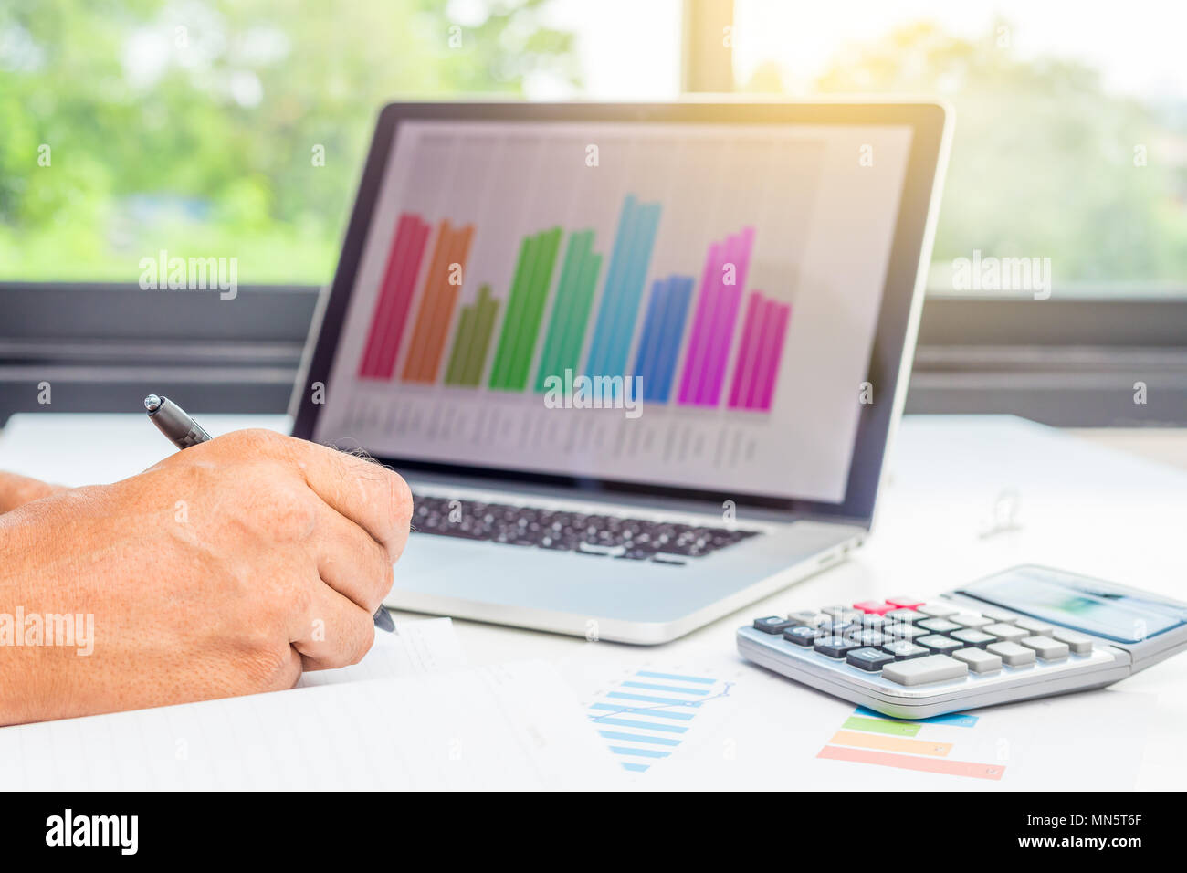 Geschäftsmann Kontrolle Bericht Gewinn auf Papier mit steigenden Charts, Nahaufnahme, Geschäftsmann, Hand mit Stift und unter Hinweis auf Papier und Laptop auf dem Schreibtisch, im Arbeitsplatz. Stockfoto