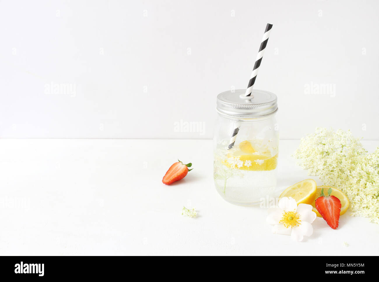 Styled Foto. Noch immer leben Zusammensetzung mit hausgemachten elderflowers Limonade in Glas trinken jar, Zitronen, Erdbeeren und wilde Rosen auf Weiß Holztisch. Sommer Garden Party Hintergrund. Stockfoto