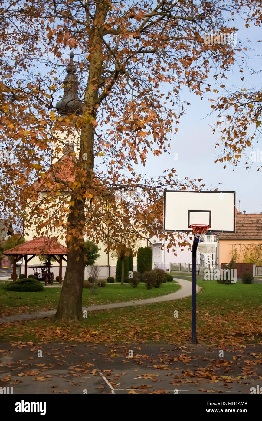 Leeren Basketballplatz im Herbst mit gelben Blätter und Kirche versteckt sich hinter Baum abgedeckt Stockfoto