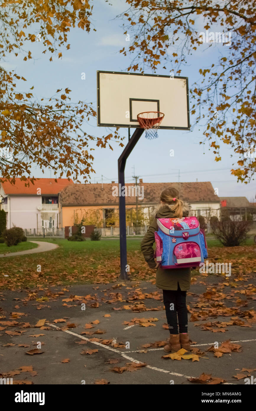 Blonde Mädchen mit ihrem rosa Schultasche auf dem Rücken am Basketballplatz beobachten, wie Blätter im Herbst fällt. Stockfoto