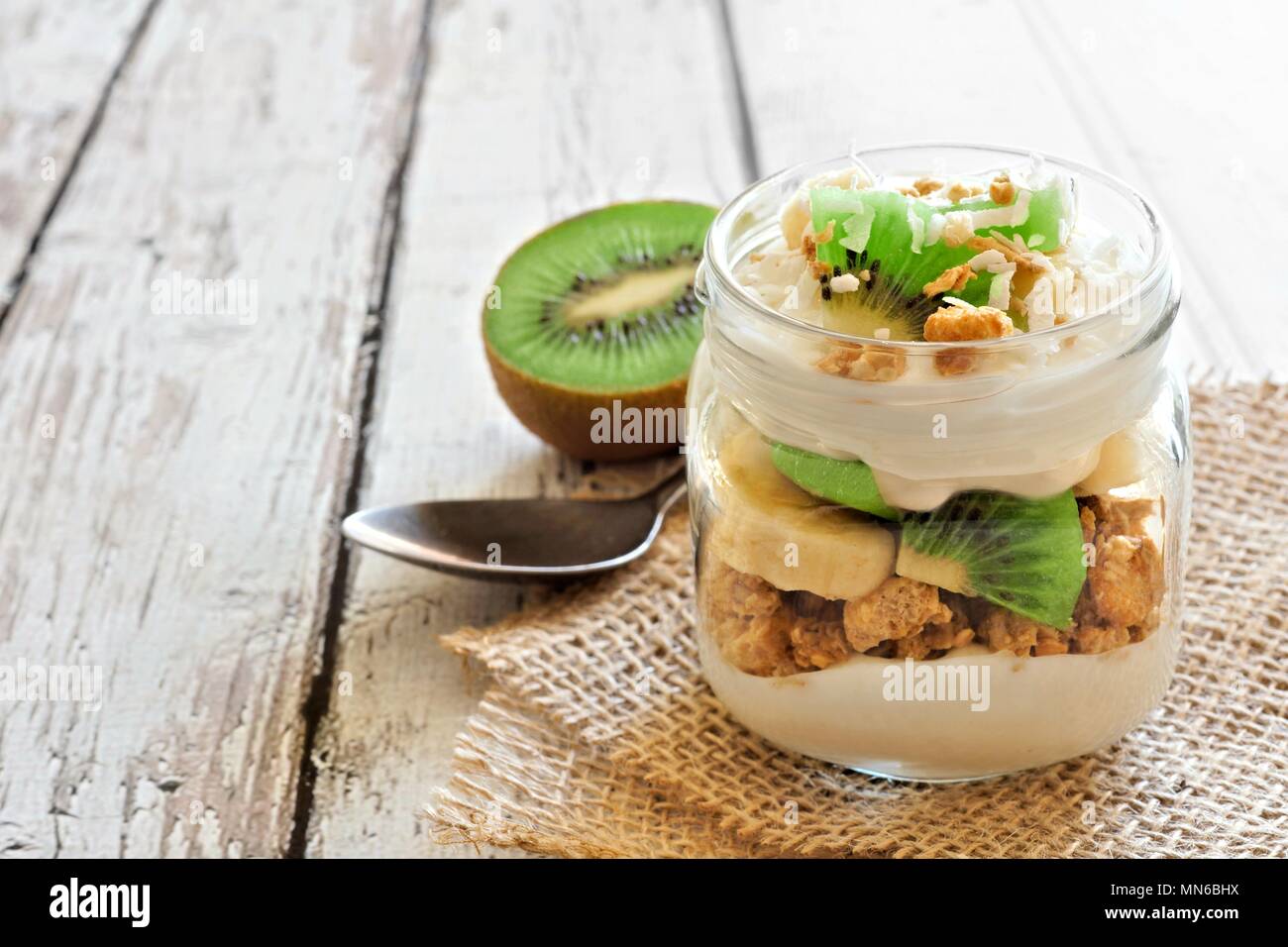 Gesunde Kiwi, Banane, coconut Parfait in einem Marmeladenglas auf einem rustikalen, mit Holz Hintergrund Stockfoto