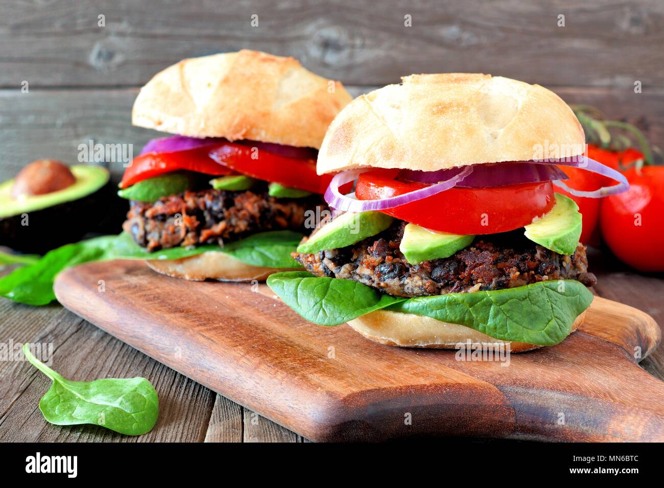 Veggie Bean und Süßkartoffel Burger mit Avocado und Spinat gegen einen rustikalen Holzmöbeln Hintergrund Stockfoto