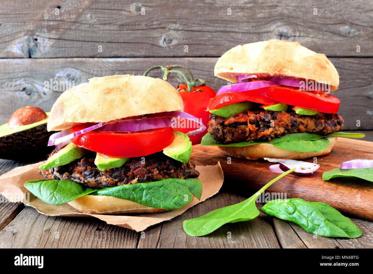 Zwei vegetarische Bean und Süßkartoffel Burger mit Avocado und Spinat gegen einen rustikalen Holzmöbeln Hintergrund Stockfoto