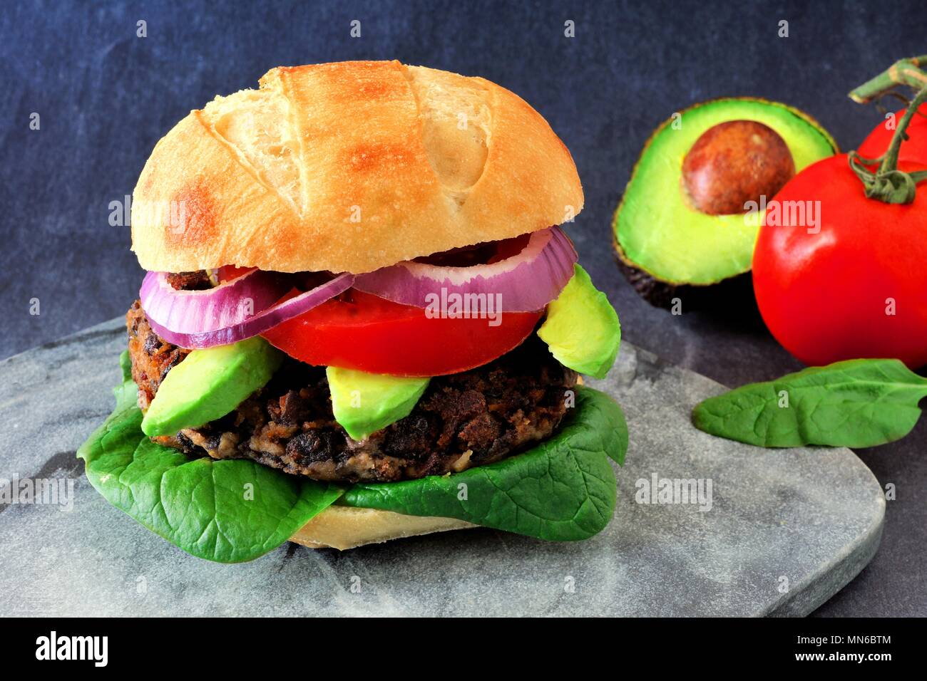 Veggie Bean und Süßkartoffel Burger mit Avocado und Spinat vor einem dunklen Hintergrund Stockfoto