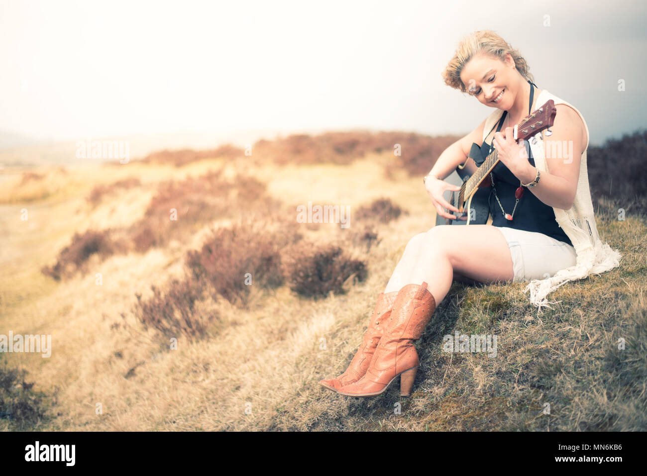 Junge Frau sitzt in einem Feld und Gitarre spielen Stockfoto