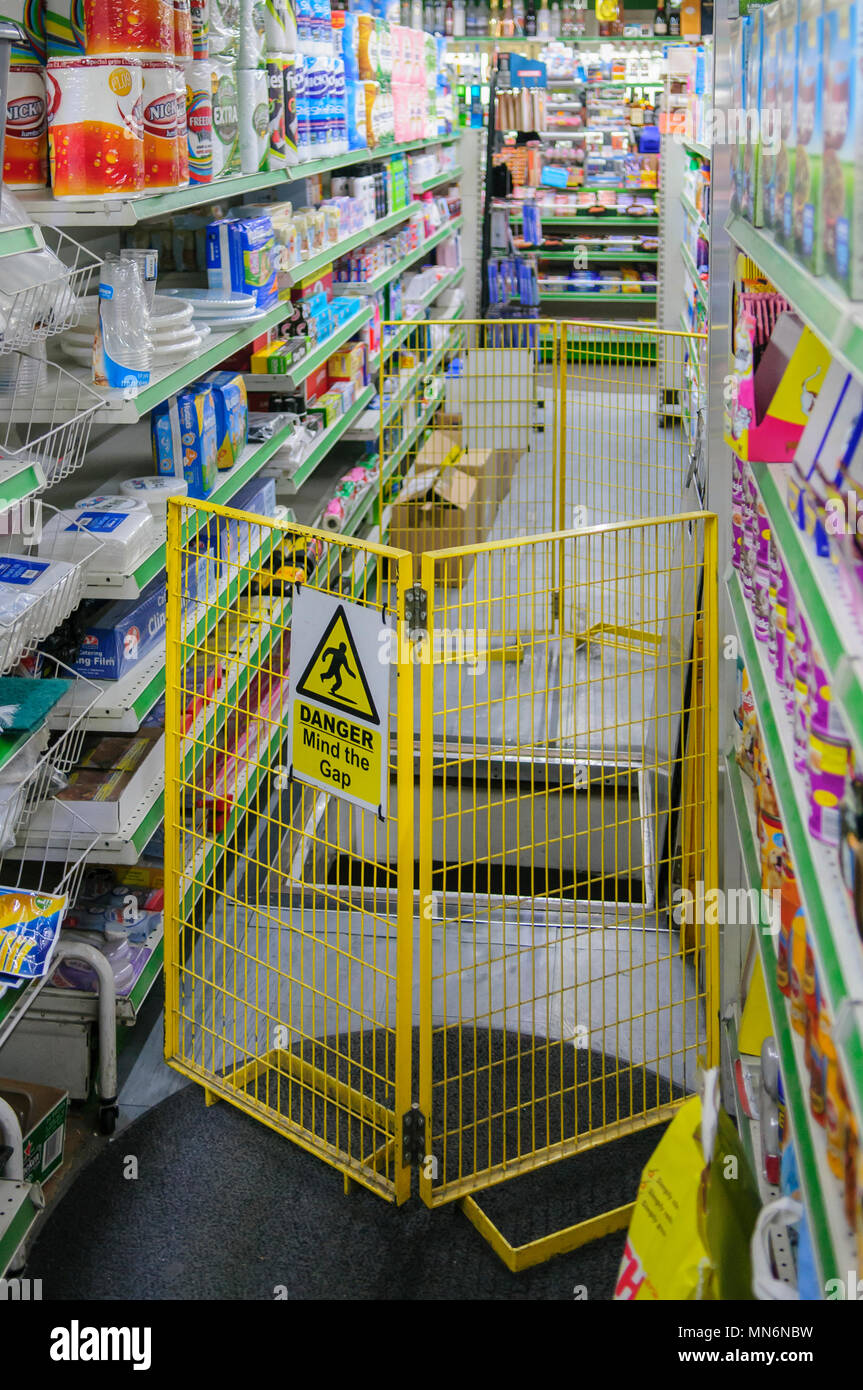 Eine gelbe Barriere mit einem Schild, auf dem "Mind the Gap) verhindert, dass Kunden fallen ein offenes Loch in ein Lebensmittelgeschäft. Stockfoto