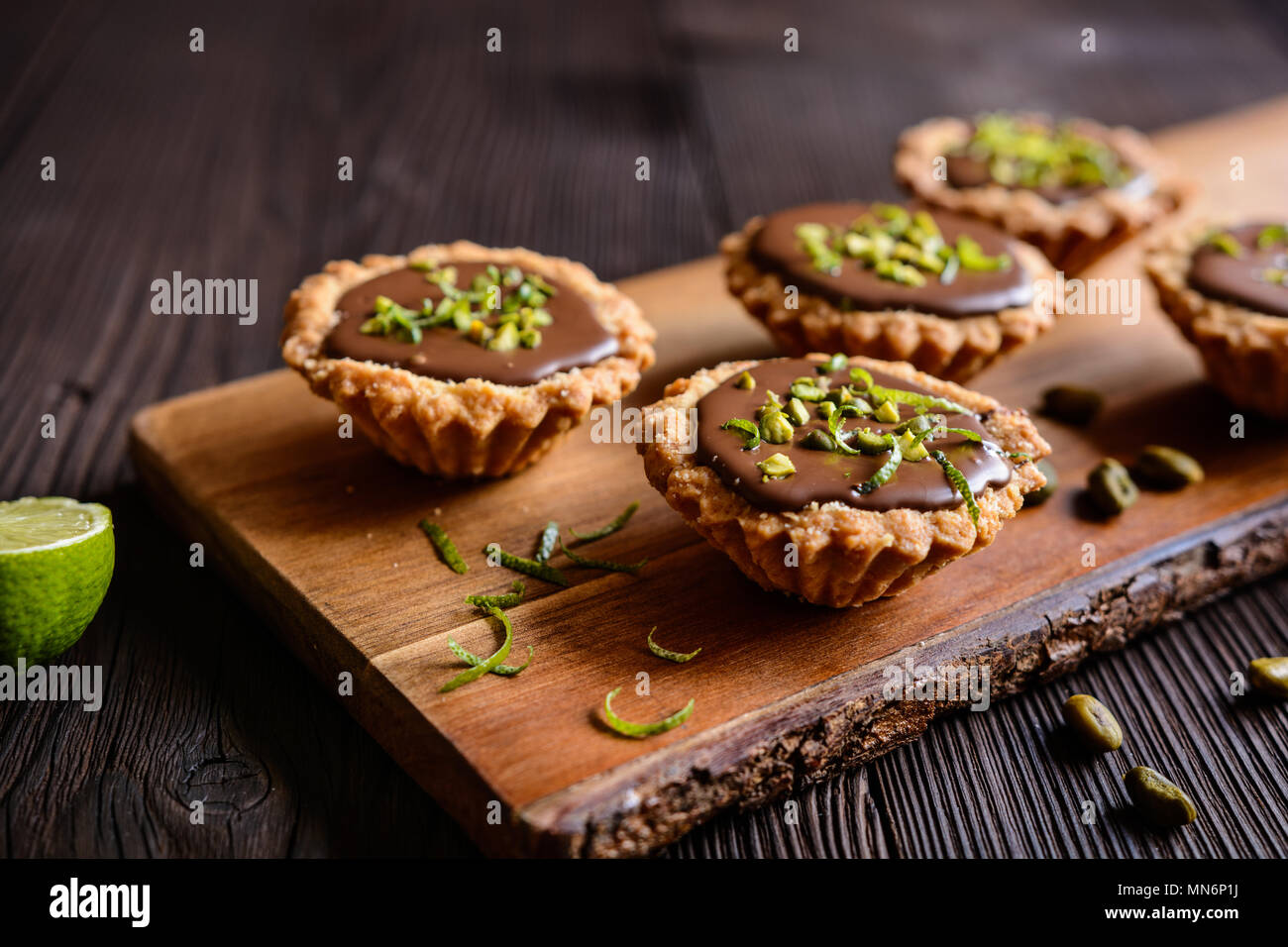 Törtchen mit Schokoladenfüllung, Pistazie und Limettenschale nachfüllen Stockfoto