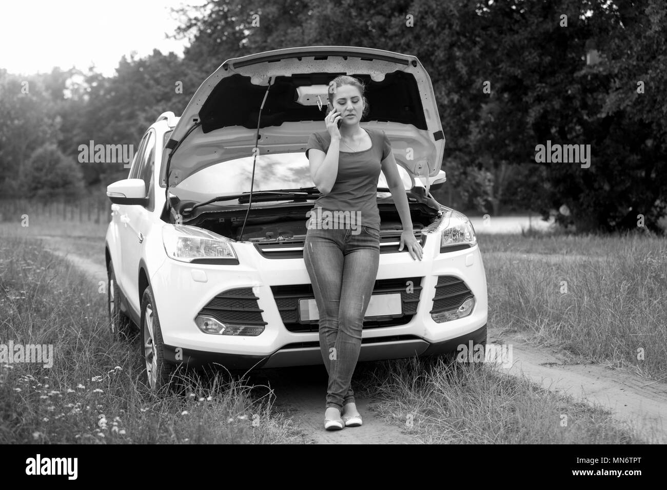 Schwarz-weiß-Bild der jungen Frau Calling Service Ihr defektes Auto im Feld zu reparieren Stockfoto
