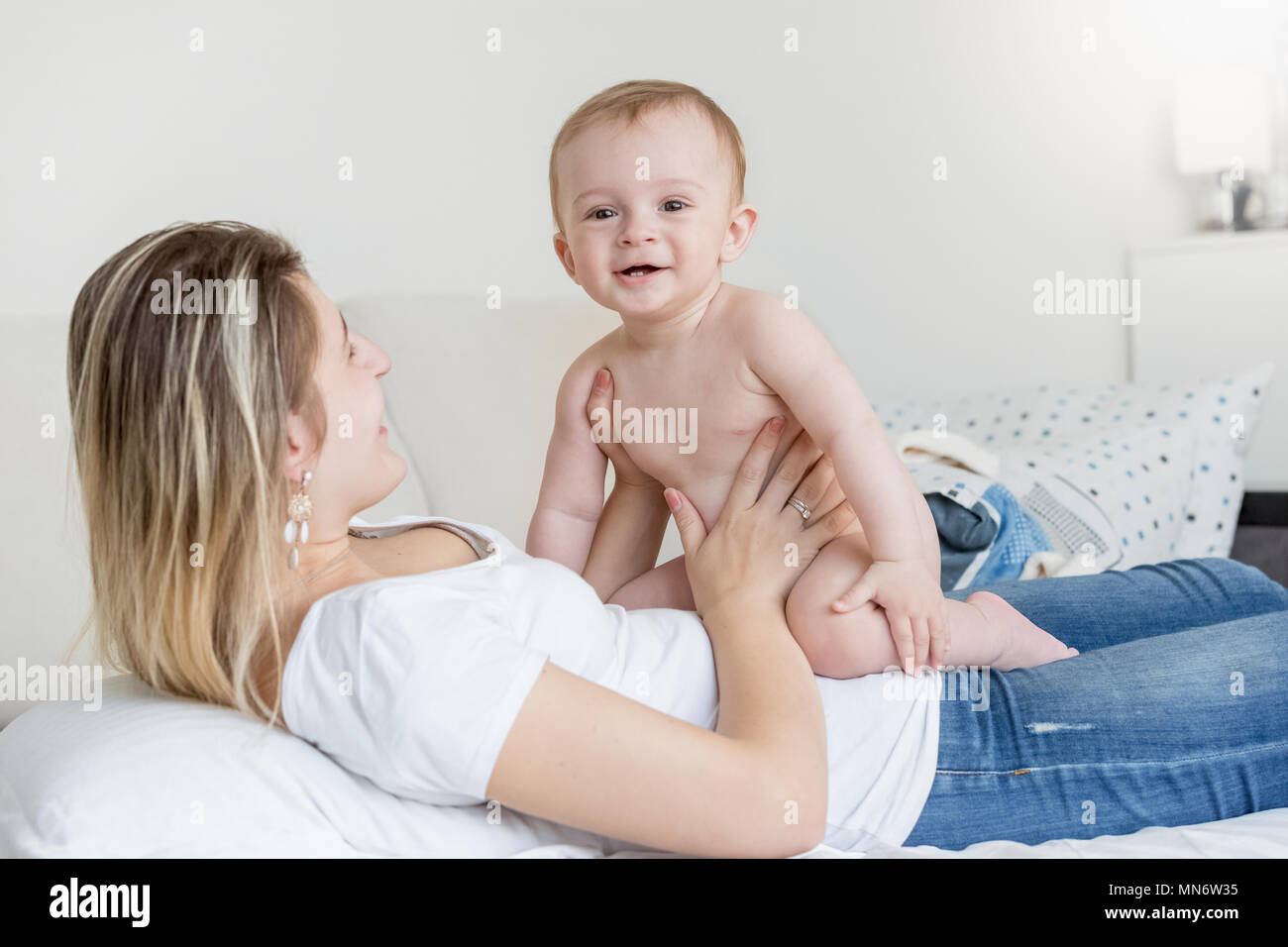 Süß lächelnde Baby Junge sitzt auf Mutter liegend auf dem Sofa im Wohnzimmer Stockfoto