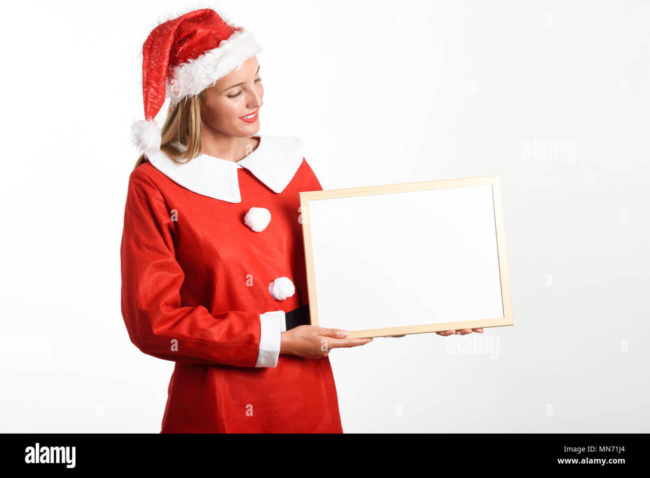 Schöne happy blonde Frau in Santa Claus Kleidung lächelnd mit White Board in den Händen. Junge Frau mit blauen Augen, isoliert auf weißem Stockfoto