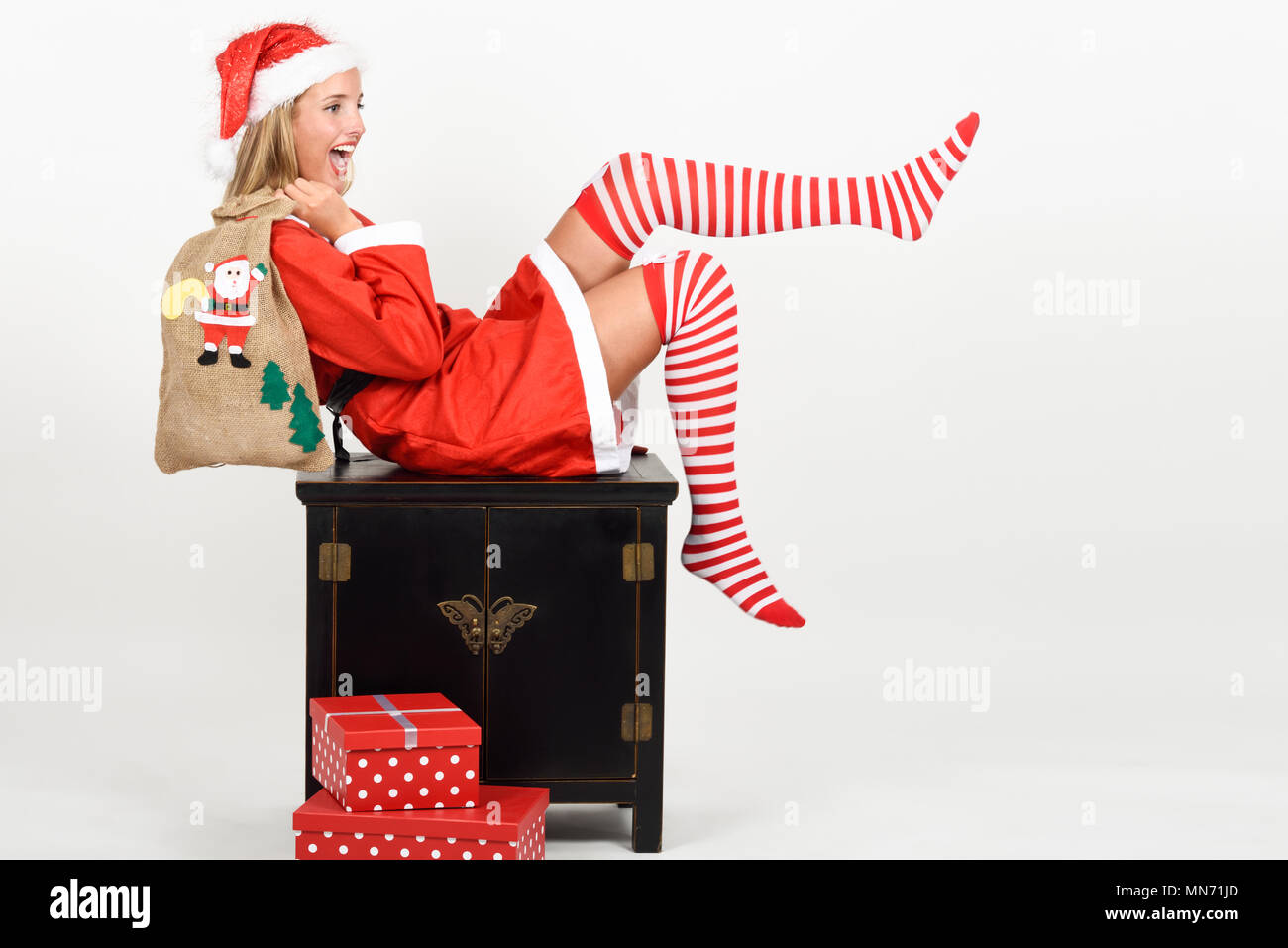 Schöne happy blonde Frau in Santa Claus Kleidung und Socken ihre Beine bewegen. Junge lustig Mädchen mit blauen Augen mit einem Sack von Santa Claus, isoliert auf weißem Stockfoto