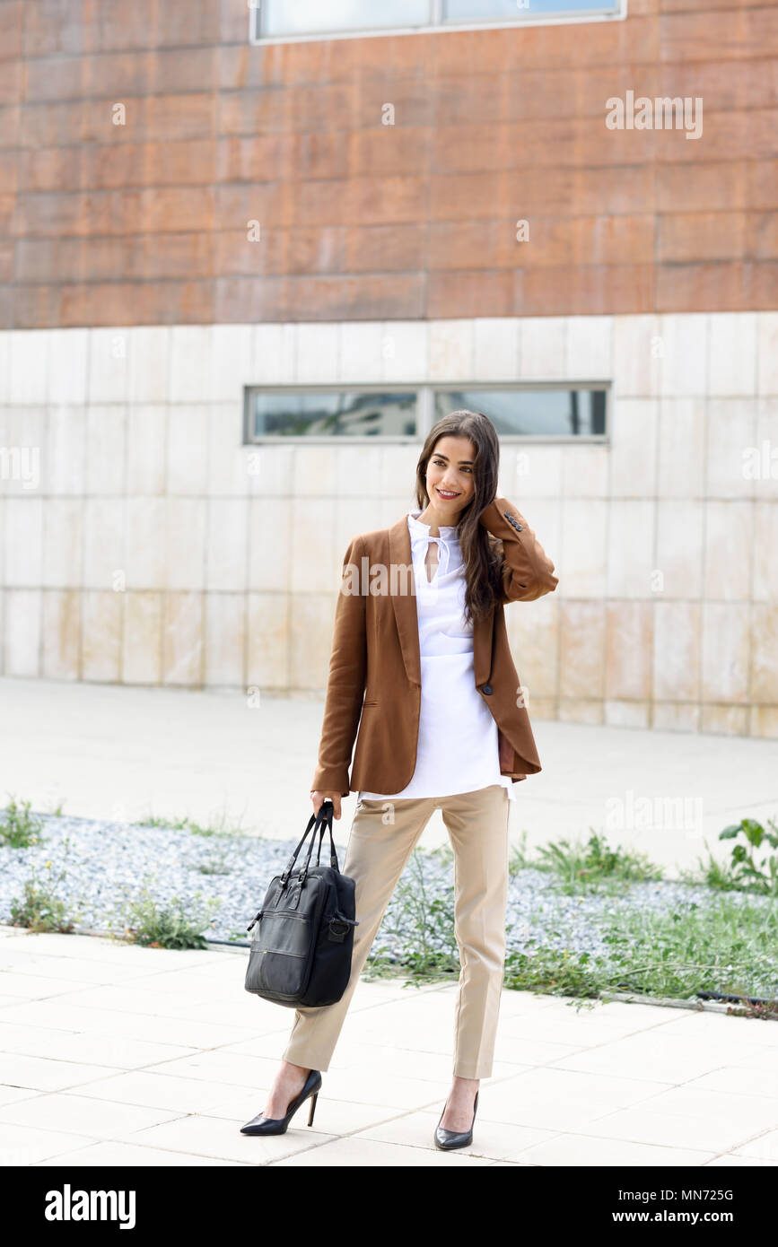 Junge Geschäftsfrau außerhalb des Bürogebäudes mit Aktenkoffer stehen. Schöne Frau tragen formalen tragen. Junges Mädchen mit braunen Jacke und Hose. Stockfoto