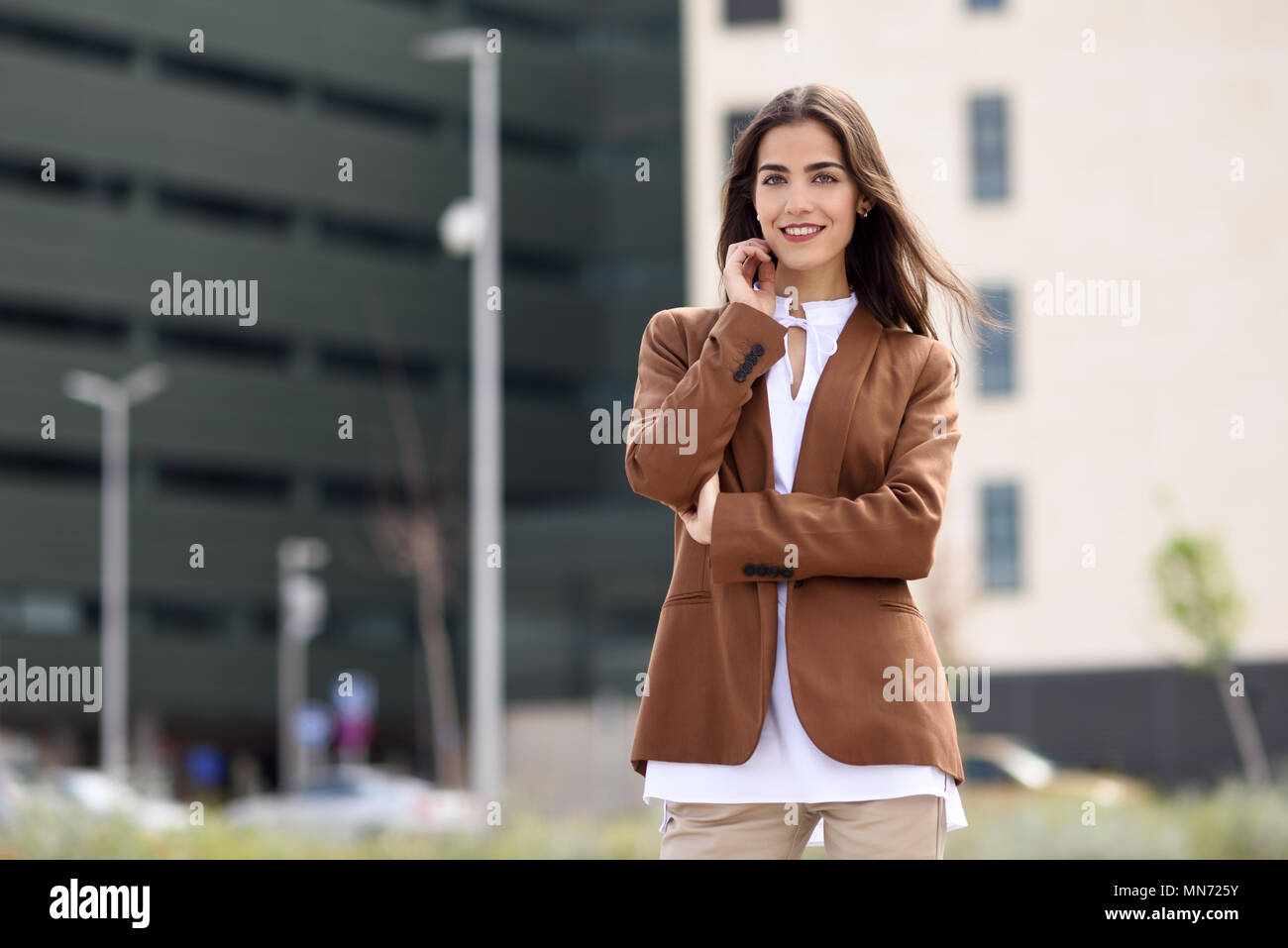 Junge Frau mit schönem Haar außerhalb des Bürogebäudes. Geschäftsfrau tragen Gesellschaftsmode mit gewellten Frisur. Junges Mädchen mit braunen Jacke und Hose. Stockfoto