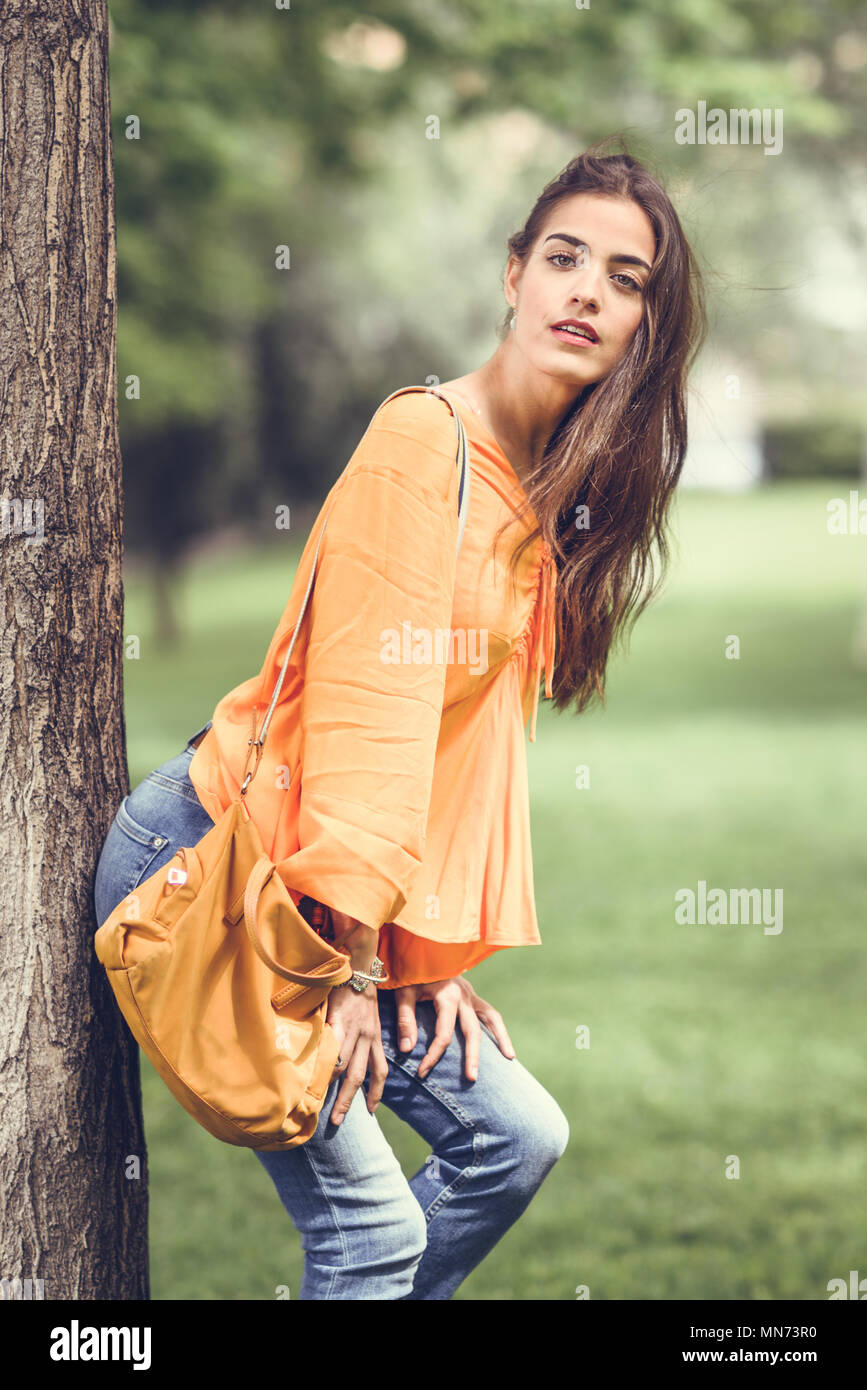 Junge Frau mit schönem Haar legere Kleidung und Tasche im städtischen Hintergrund. Happy girl mit gewellten Frisur in einem Park in der Stadt. Stockfoto