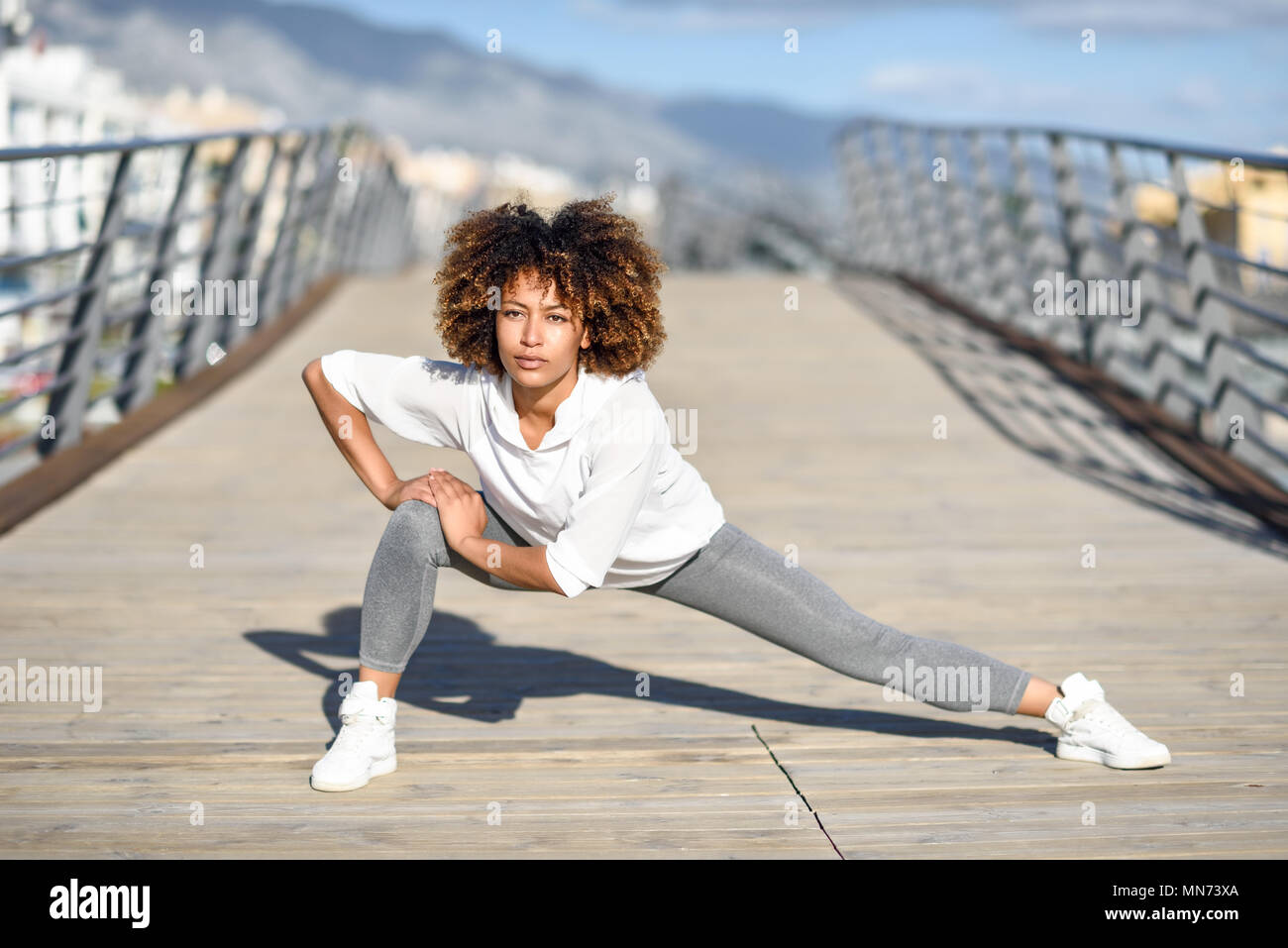Junge schwarze Frau zu tun Stretching nach draußen. Mädchen trainieren mit City scape im Hintergrund. Afro Haar. Stockfoto