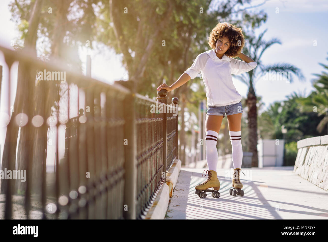 Junge schwarze Frau auf Rollschuhen reiten in der Nähe vom Strand. Mädchen mit Afro Frisur rollerblading an sonnigen Promenade mit Hintergrundbeleuchtung. Stockfoto
