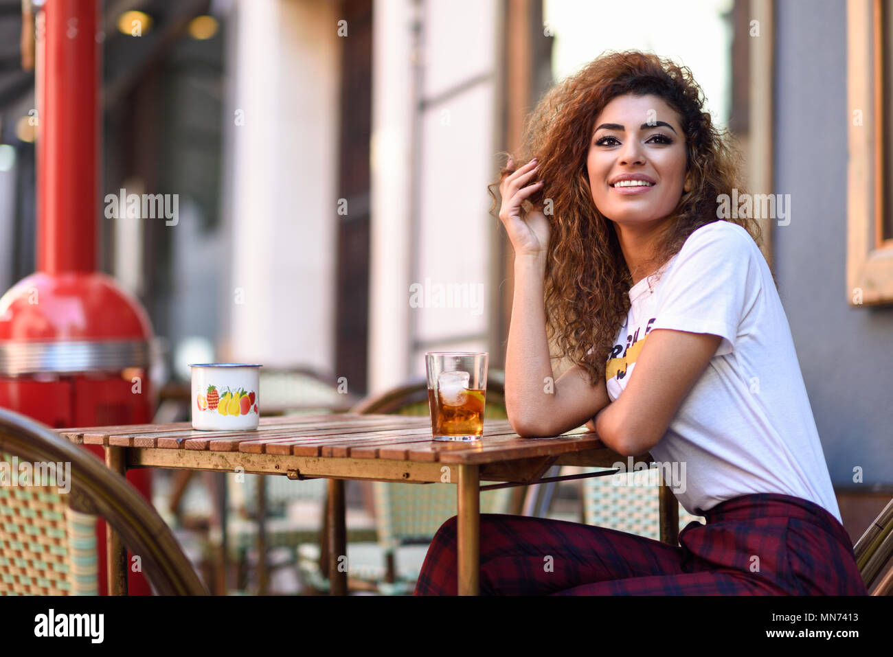 Junge arabische Frau lächelnd und sitzen in einer Bar in der Straße. Arabische Mädchen in legere Kleidung trinken ein Soda im Freien. Stockfoto