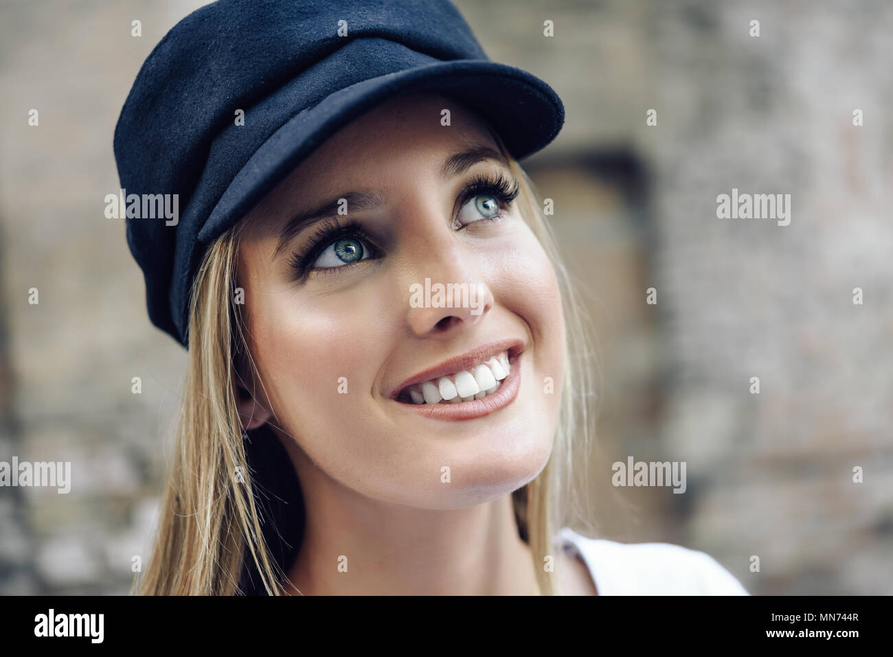 Junge blonde Frau im Defokussierten im städtischen Hintergrund. Mädchen mit blauen Augen tragen Cap. Stockfoto