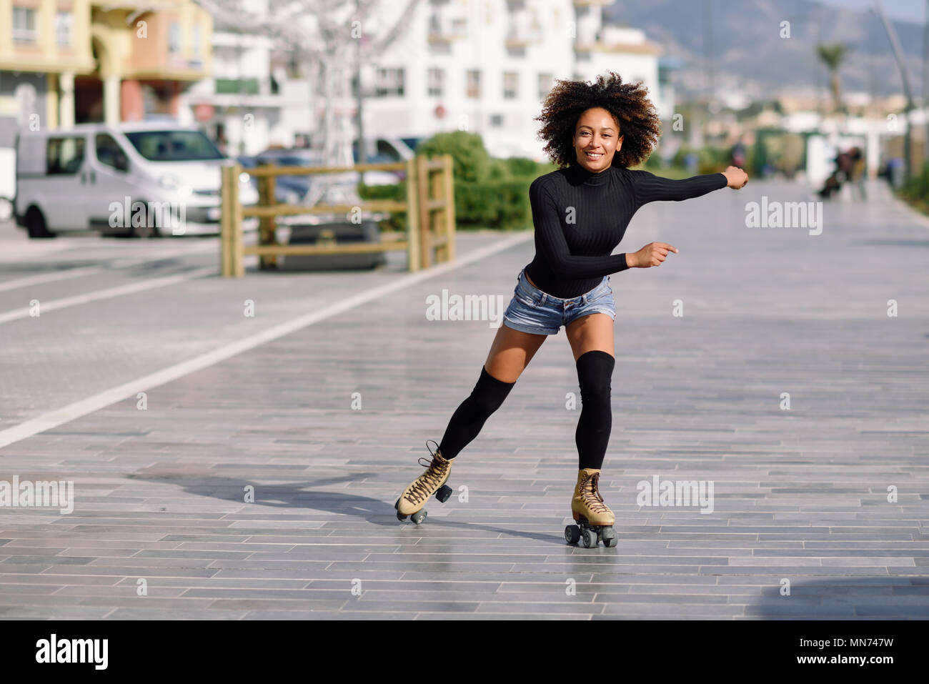 Junge passen schwarze Frau auf Rollschuhen reiten im Freien auf Urban Street. Lächelnde Mädchen mit Afro Frisur rollerblading an einem sonnigen Tag Stockfoto