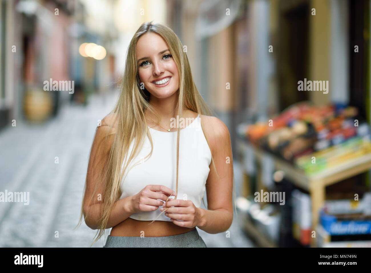 Lächelnde junge Frau im städtischen Hintergrund. Blonde Mädchen tragen mit schönes Haar legere Kleidung auf der Straße. Gerade Frisur. Stockfoto