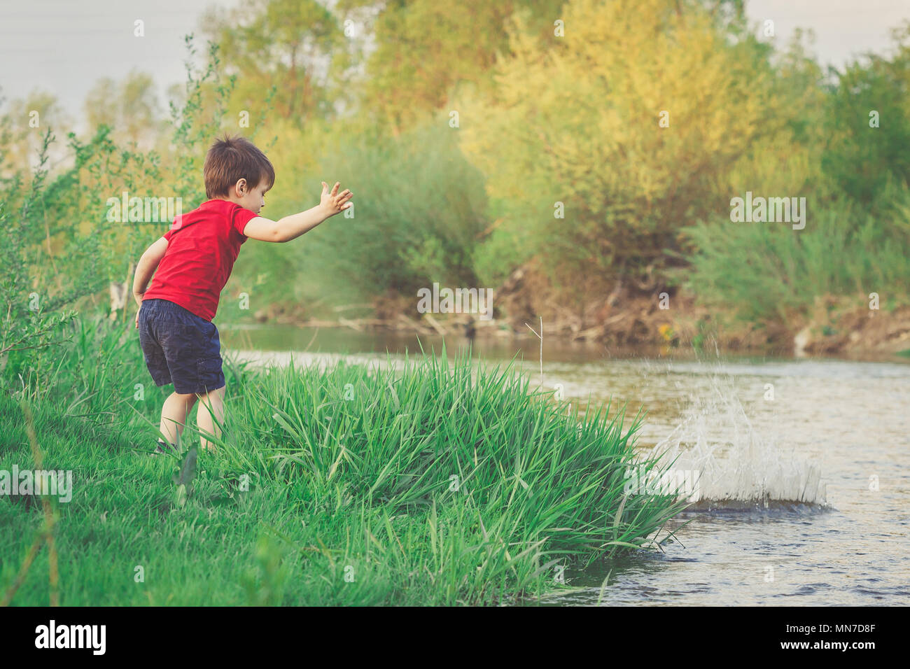 Wenig Junge wirft einen Stein ino den Fluss. Sommer Urlaub Aktivitäten Stockfoto