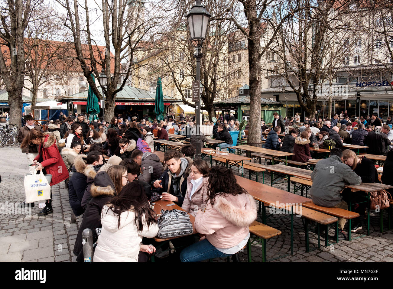 Auf einem März Sonntag Morgen, der Biergarten am Viktualienmarkt in München beschäftigt sich mit vorwiegend jungen Menschen Stockfoto