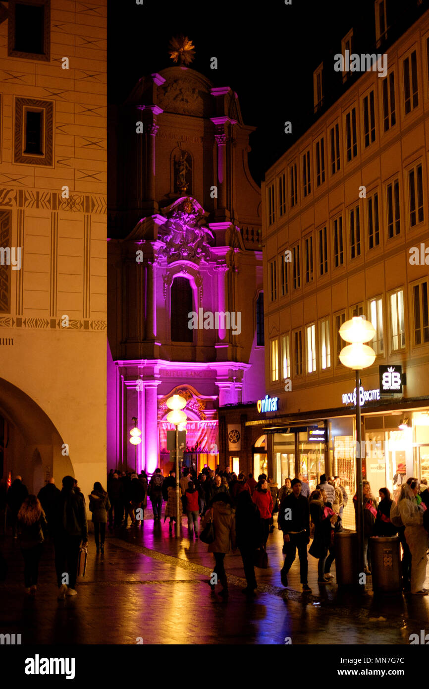 An der Ecke einer lebhaften Marienplatz an einem Samstag Abend im März, die Heiliggeistkirche Kirche ist in ein rosafarbenes Licht getaucht Stockfoto