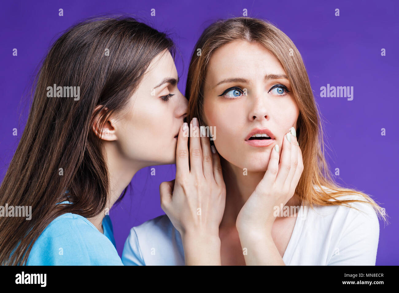 Zwei hübsche Frauen gossipping mit Gesicht Reaktion Ausdruck vor blauem Hintergrund Stockfoto