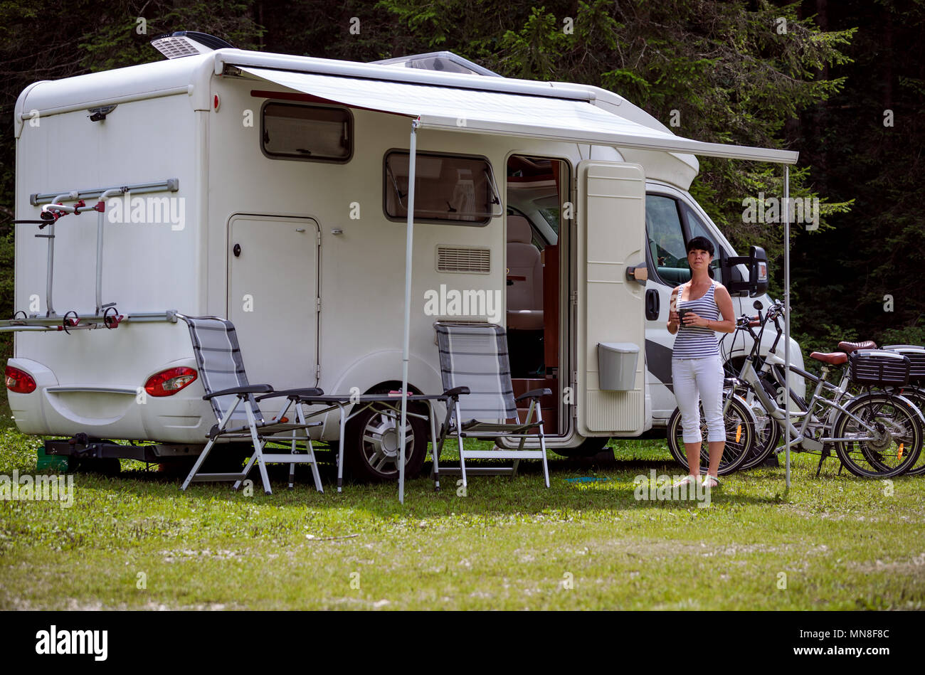 Frau steht mit einem Becher Kaffee in der Nähe der Camper. Caravan Auto Urlaub. Familie Urlaub Reisen, Urlaub im Reisemobil RV Stockfoto