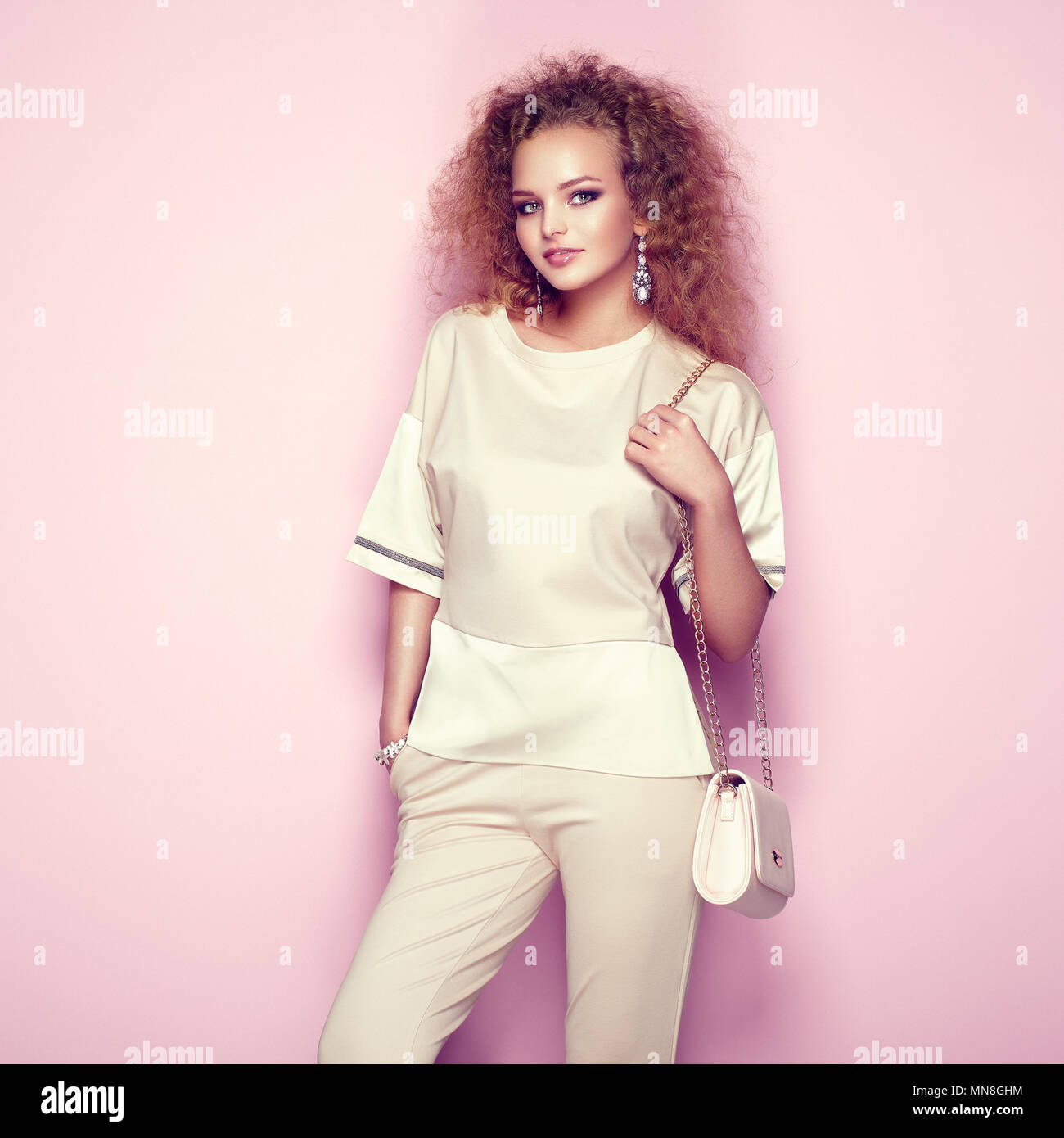 Mode Portrait von einer Frau im Sommer Outfit. Girl posiert auf rosa Hintergrund. Rosa Handtasche. Stilvolle curly Frisur. Glamour lady Stockfoto